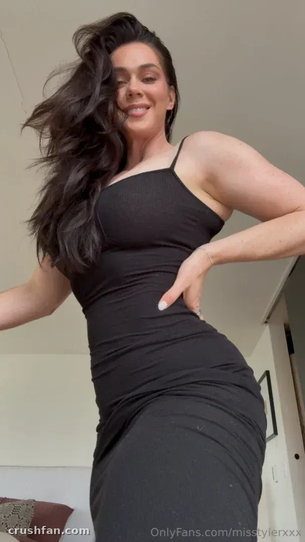 Alison Tyler in a fitted black dress standing indoors with her hair swept to one side