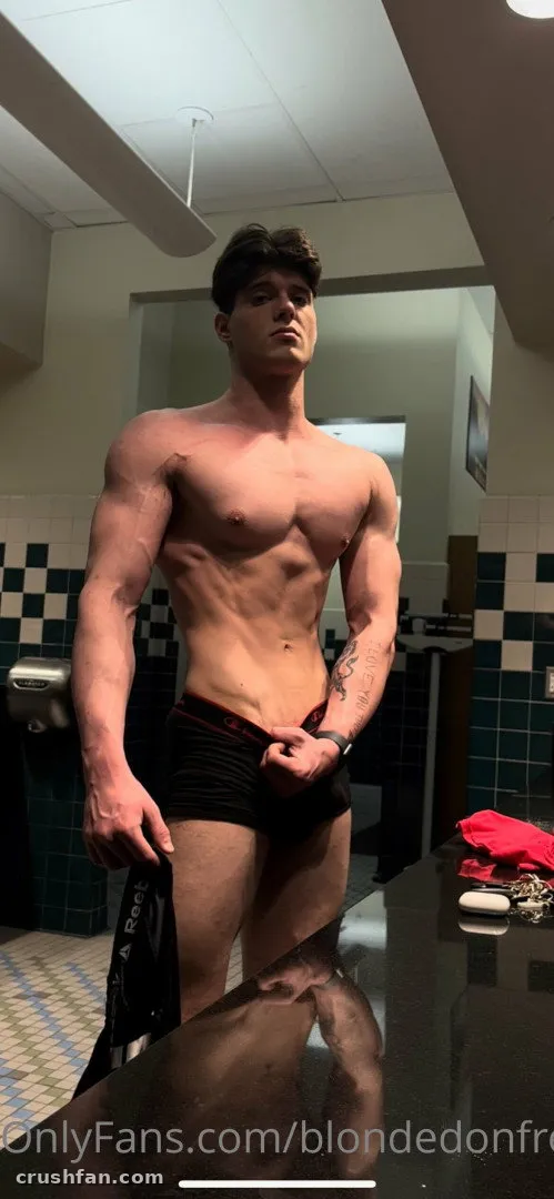 Shirtless man in dark briefs posing in a tiled changing room mirror selfie