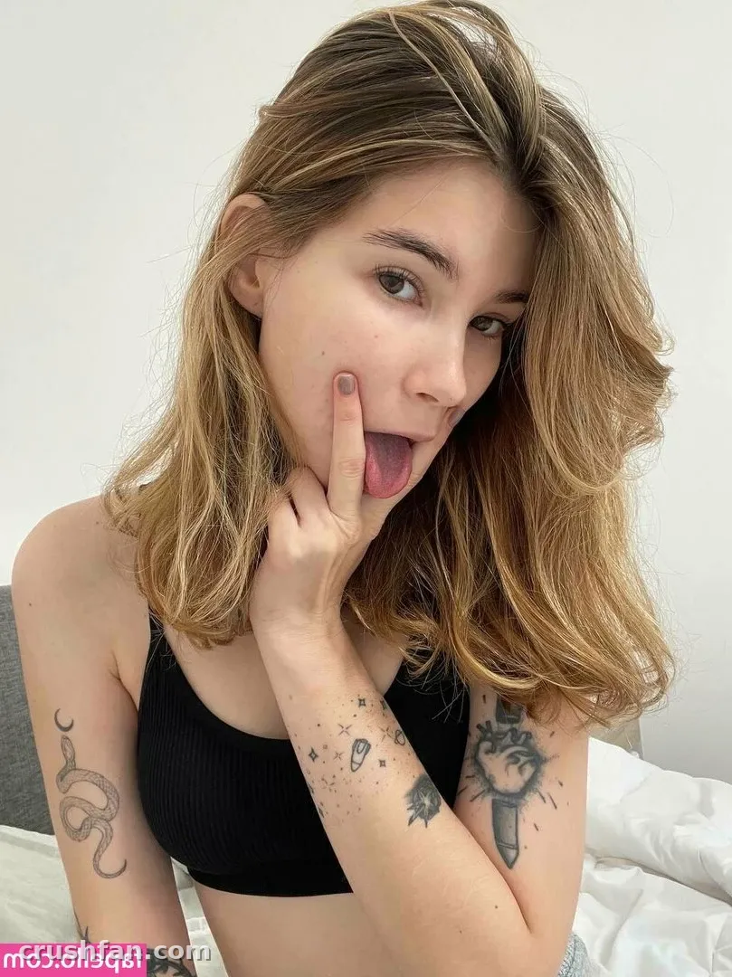 Anicka com um top preto tirando uma selfie divertida contra uma parede branca