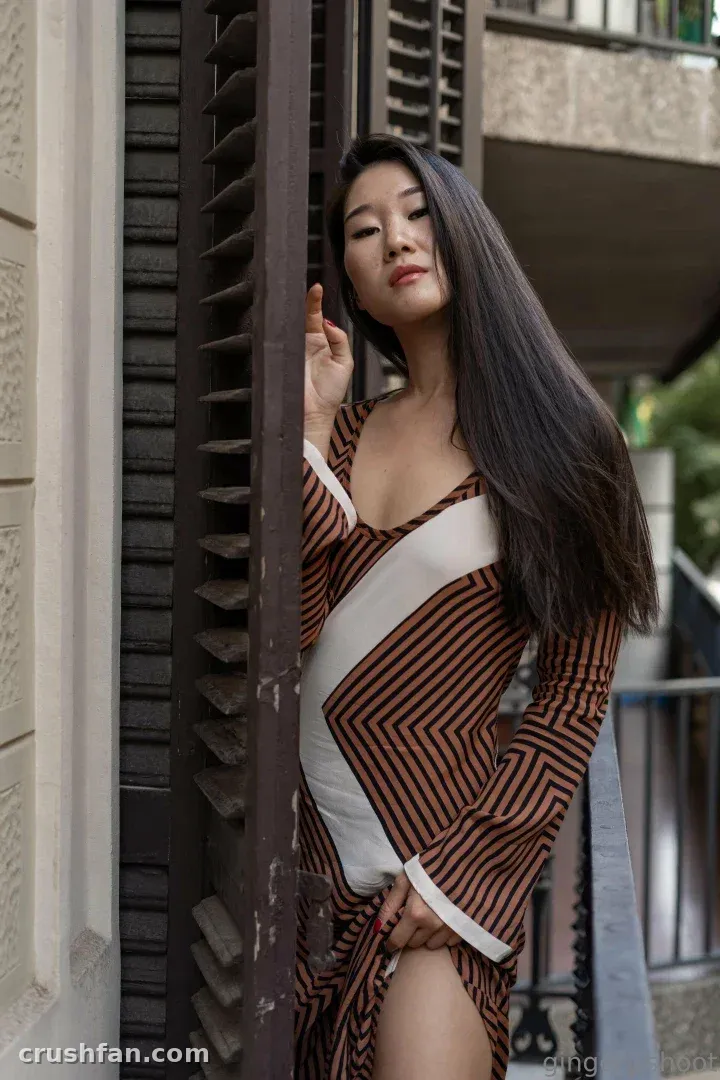 Gingery shoot in a striped wrap dress standing by dark wooden shutters outdoors