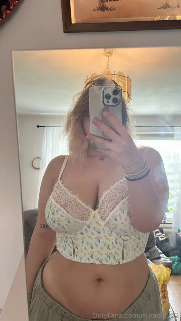 Mika22 prenant un selfie miroir dans un bralette en dentelle florale et un pantalon gris