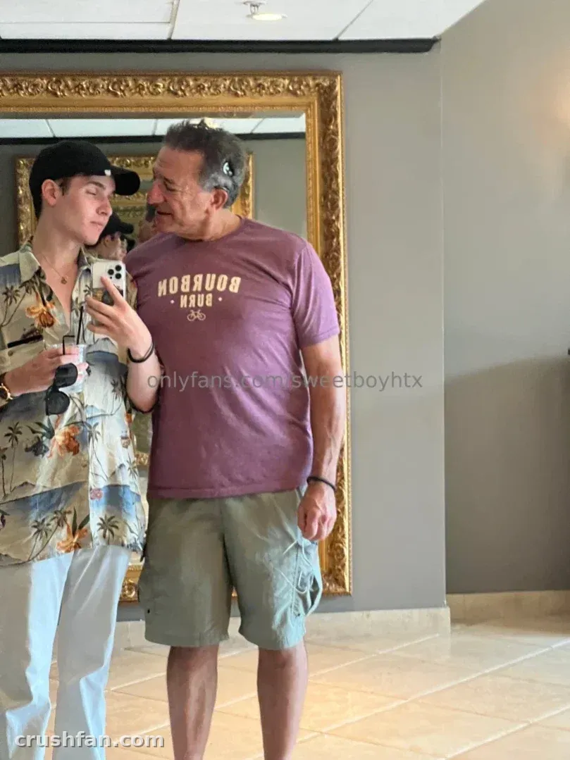 Sweet Boy con una camisa floral de pie junto a un gran espejo dorado en el interior.