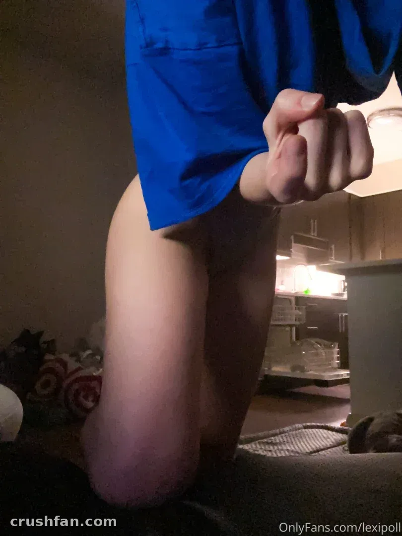 Creator kneeling indoors in a loose blue shirt under dim warm light