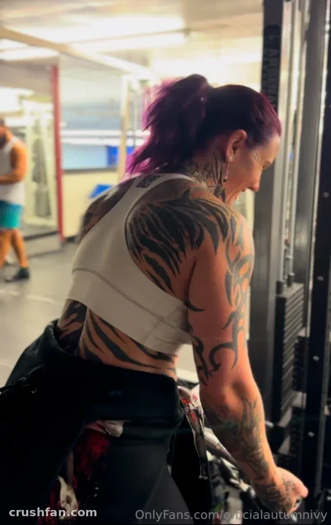 Tattooed woman in a grey crop top standing by gym equipment