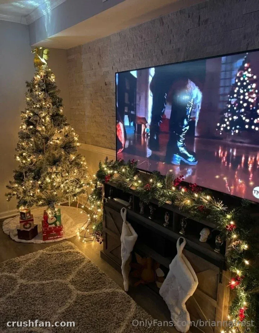 Festive living room with a lit Christmas tree, garland and stockings near a television.