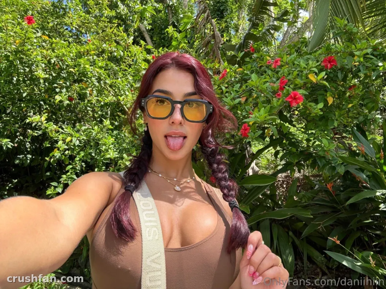 Dani ♥️ in einem sonnigen Garten mit bernsteinfarbener Sonnenbrille und taupefarbenem Oberteil, Haare in Zöpfen