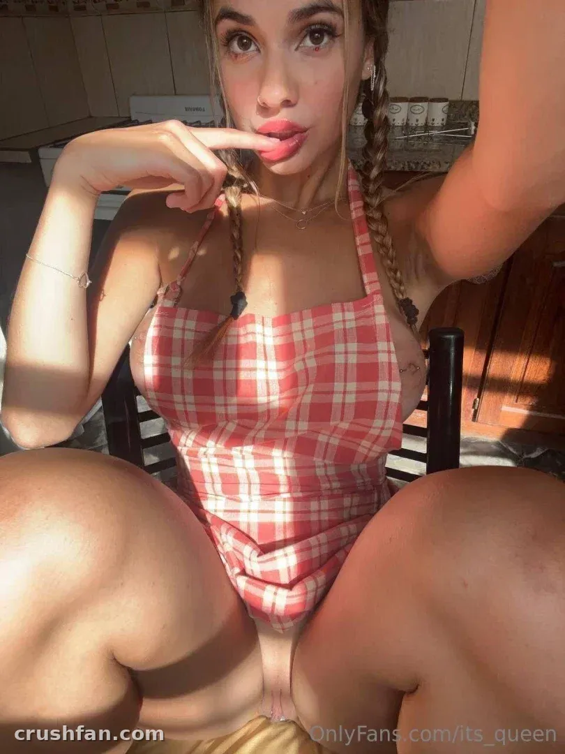 Wet Pussy con un top de cuadros rojo y el pelo trenzado sentada en una silla de madera en interiores