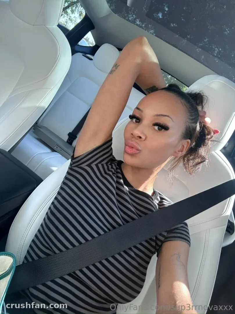 Créatrice en haut rayé assise dans une voiture avec la ceinture de sécurité en travers de la poitrine, le bras levé derrière la tête.