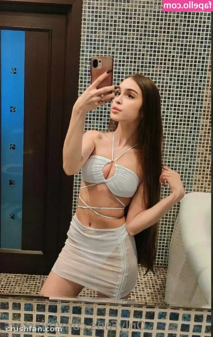 Mia prend un selfie dans le miroir dans un ensemble deux pièces bleu pâle devant un mur carrelé de mosaïque