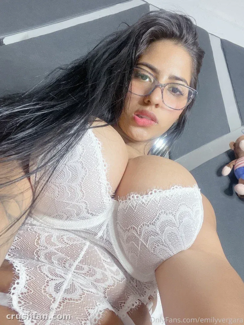 Criadora com um body de renda branca e óculos tirando uma selfie de perto em ambiente interno.