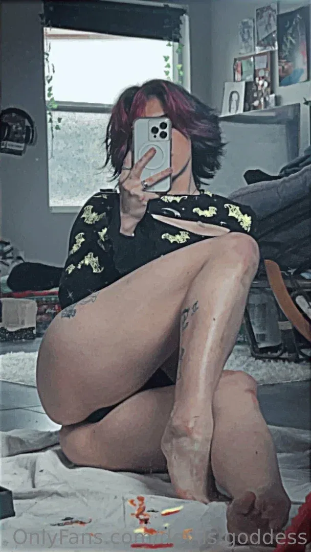 Tovi tira uma selfie no espelho enquanto senta de pernas cruzadas em um quarto com pouca luz