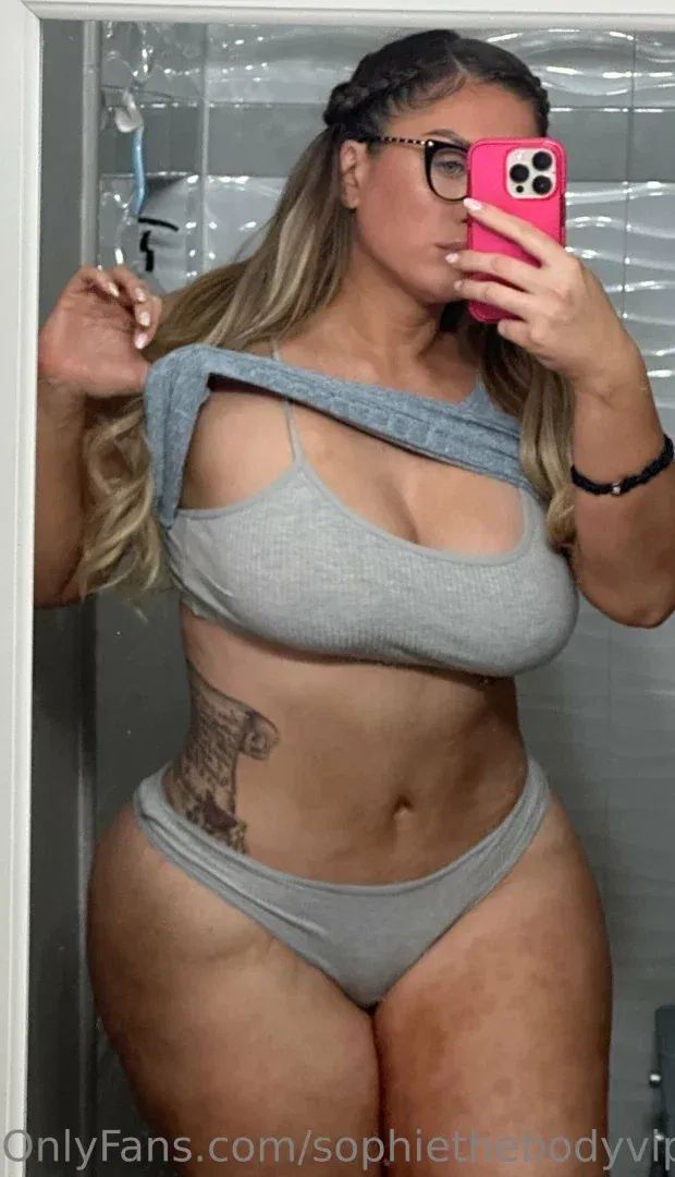 Sophie VIP Tall Girl tirando uma selfie no espelho com roupa de descanso cinza e um celular rosa.