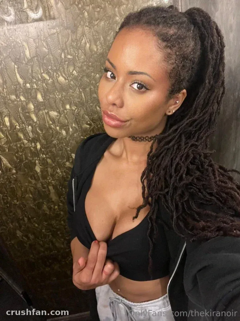 Kira Noir dans un haut noir posant devant un mur à texture dorée