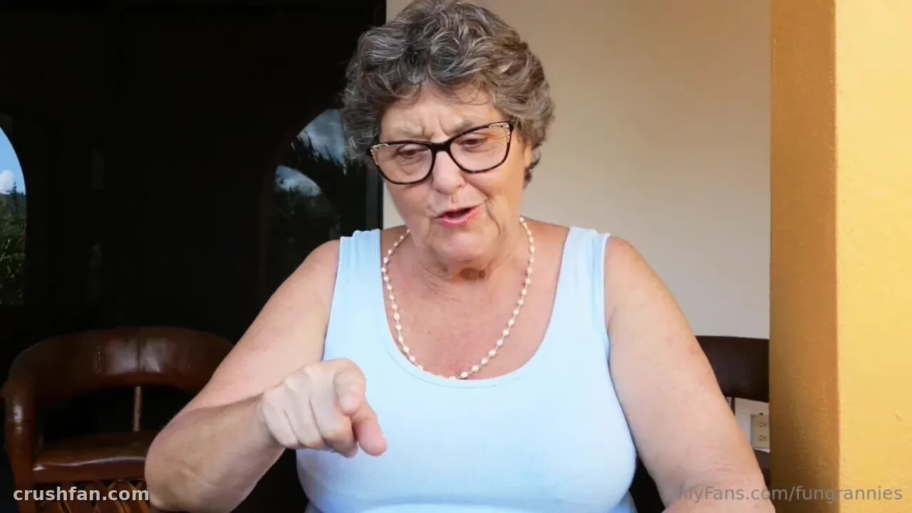 Fungrannies in a pale blue tank top and glasses pointing at the camera indoors