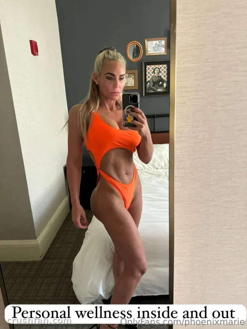 Phoenix Marie con un bañador naranja tomándose una selfie frente al espejo en una habitación de hotel