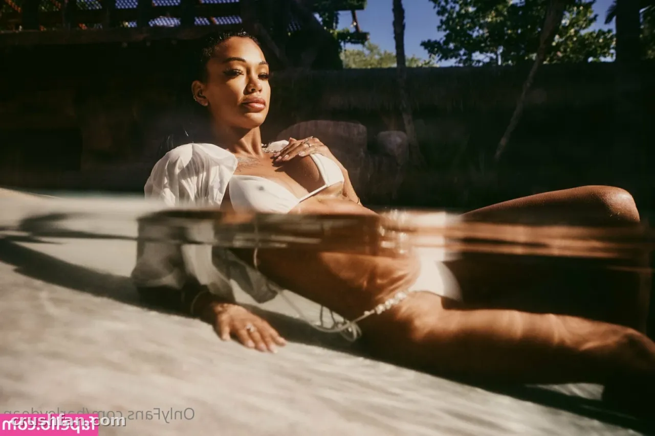 Creadora con bikini blanco y camisa abierta recostada junto a una piscina bañada por el sol.
