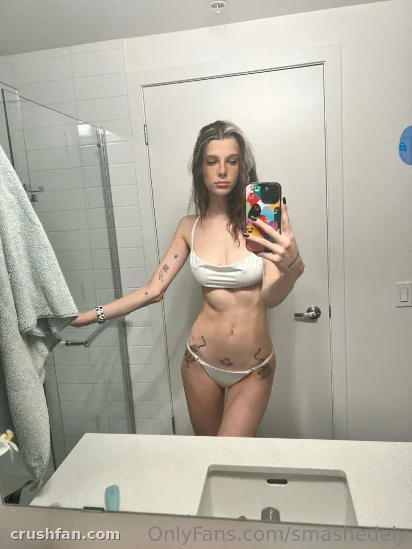 Smashedely tomándose una selfie en el espejo con un conjunto de dos piezas blanco en un baño