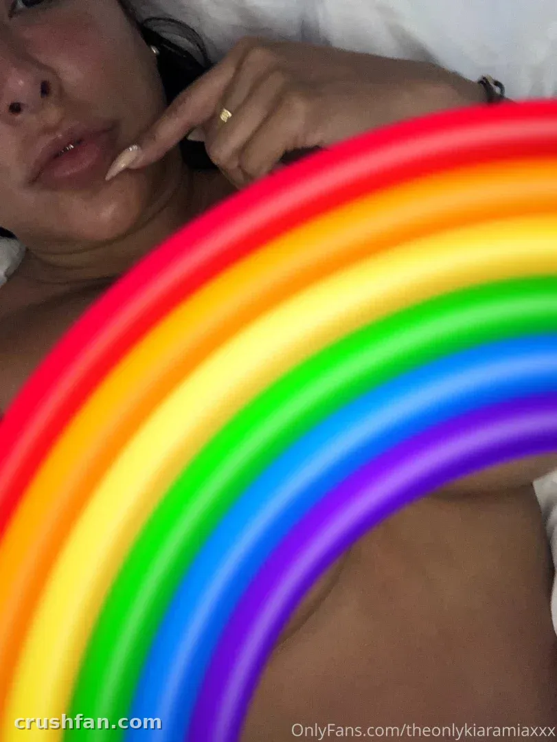Creator resting on white bedding behind a large colourful inflatable rainbow