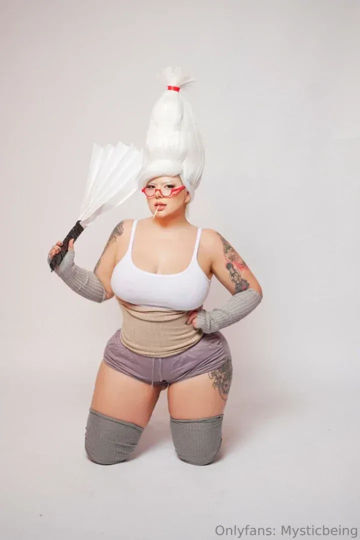 Creator MysticBeing kneeling in a white wig, red glasses and grey outfit while holding a white fan.