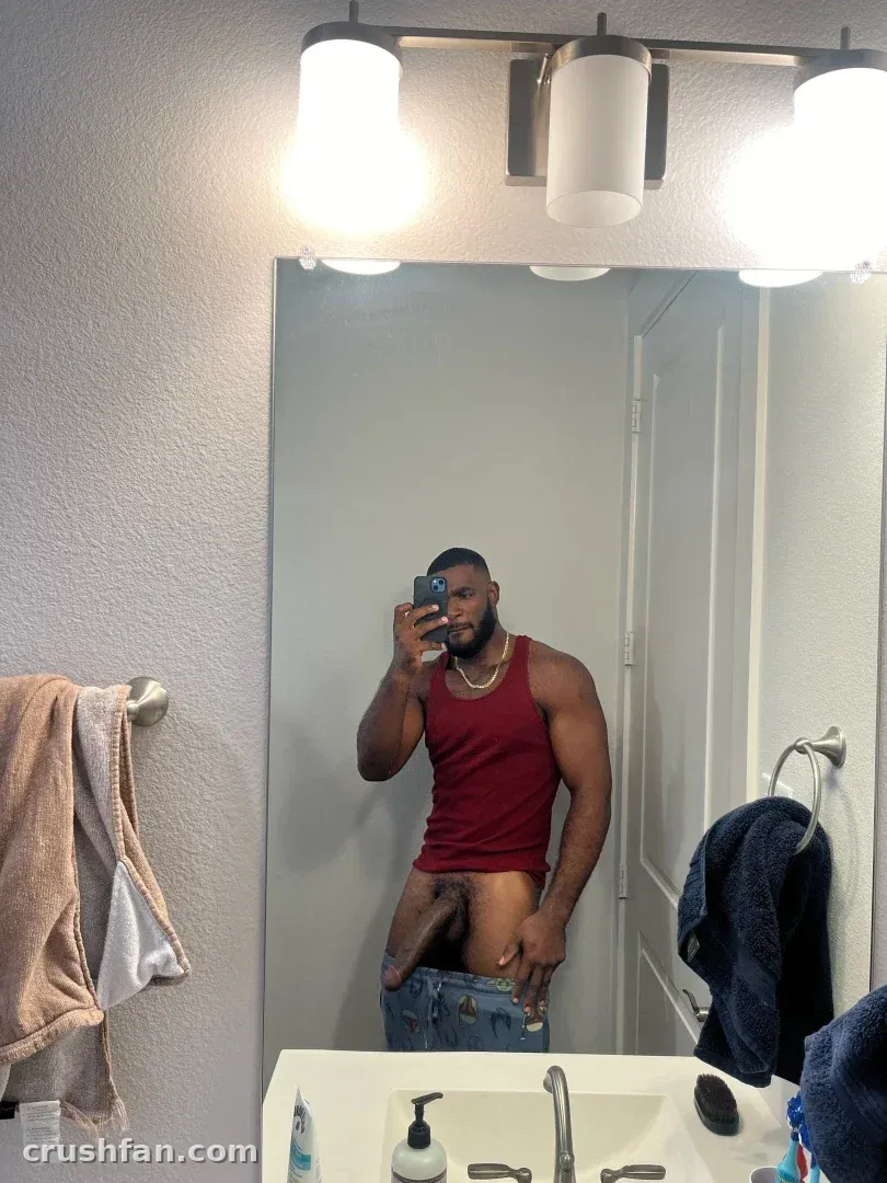 Marshall Price taking a mirror selfie in a bright bathroom while wearing a red tank top and jeans.