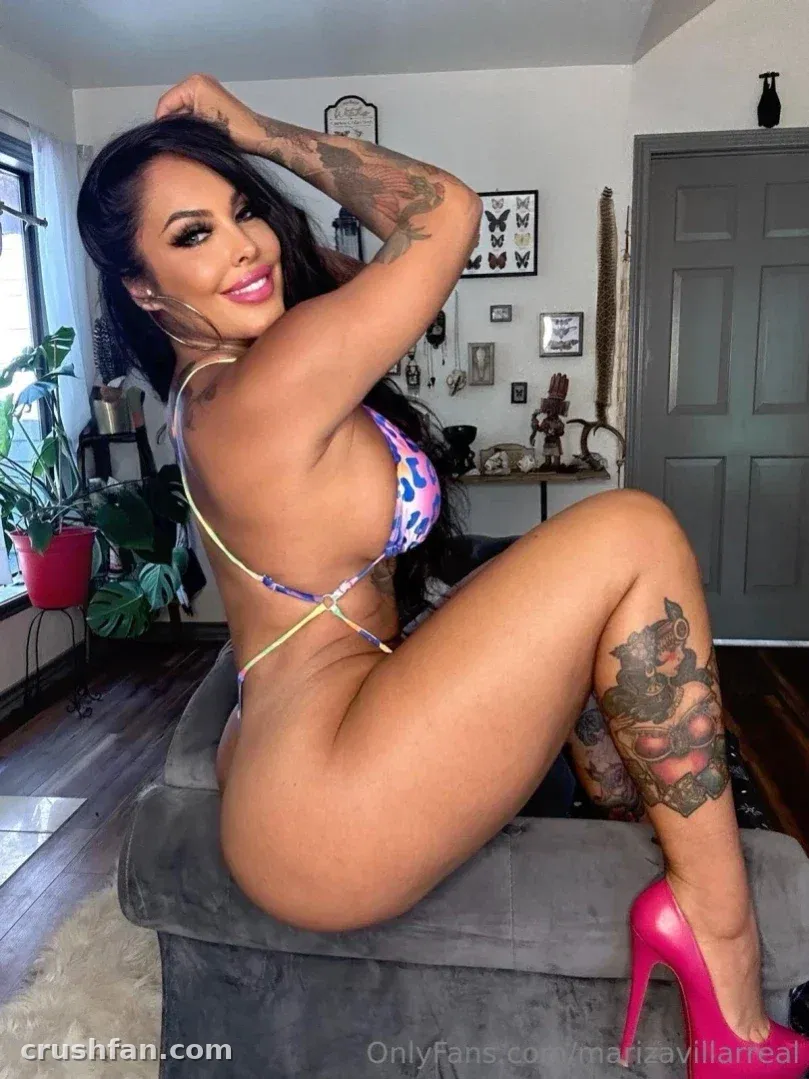 Mariza Villarreal com um biquíni estampado e saltos rosa sentada em uma cadeira cinza em ambiente interno