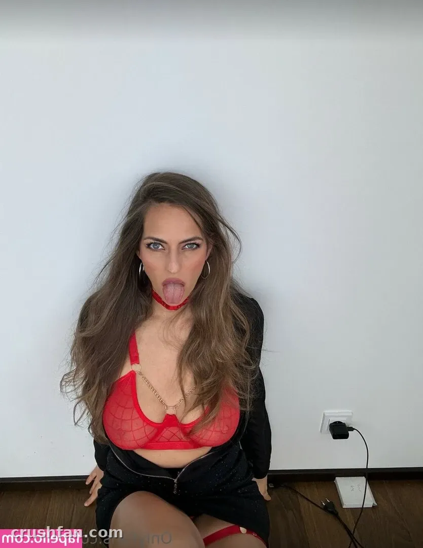 LUSILOVE kneeling in red lace lingerie and a black skirt against a white wall