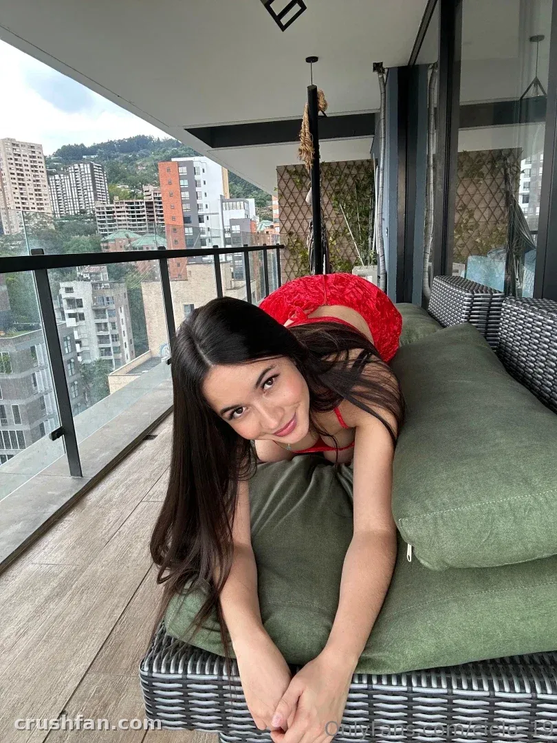 Mujer con un atuendo rojo recostada en una tumbona de balcón con el horizonte de una ciudad detrás de ella