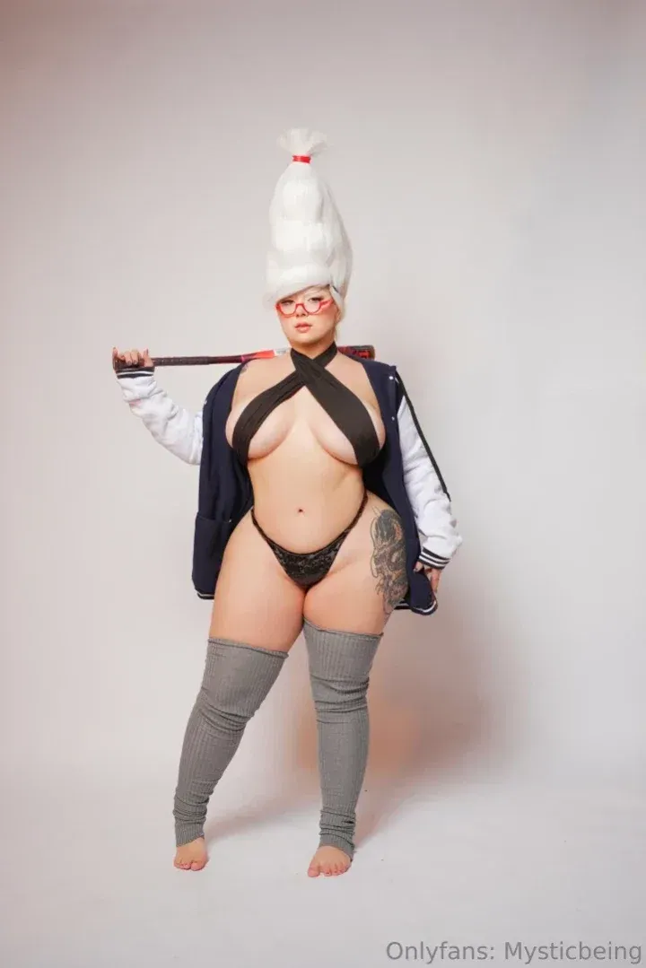 MysticBeing in a cosplay-inspired outfit with a tall white wig against a grey studio backdrop.