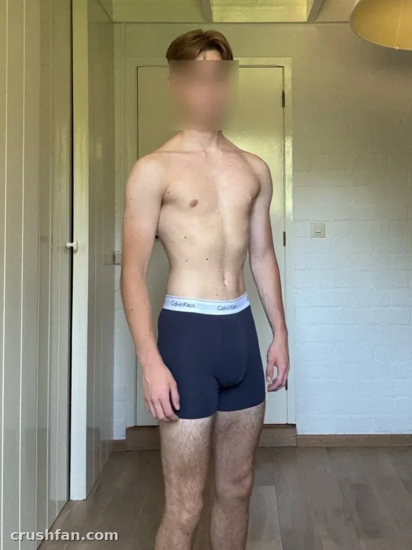 Manu steht in einem hellen Flur und trägt dunkle Boxershorts