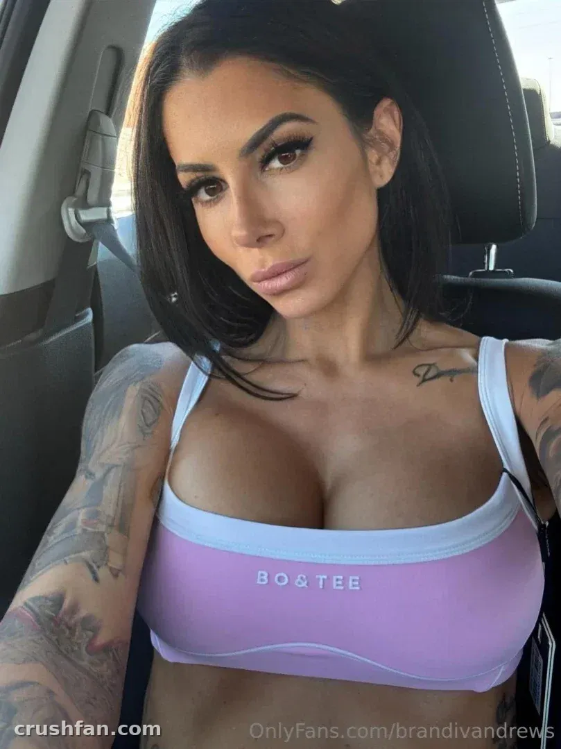 Brandi Andrews taking a close-up selfie inside a car wearing a lavender and white sports top