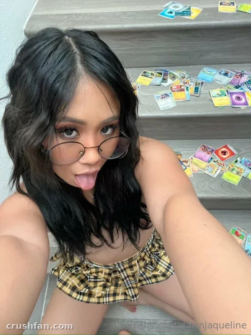 Dawn Jaqueline in a plaid skirt and glasses sitting on carpeted stairs with trading cards