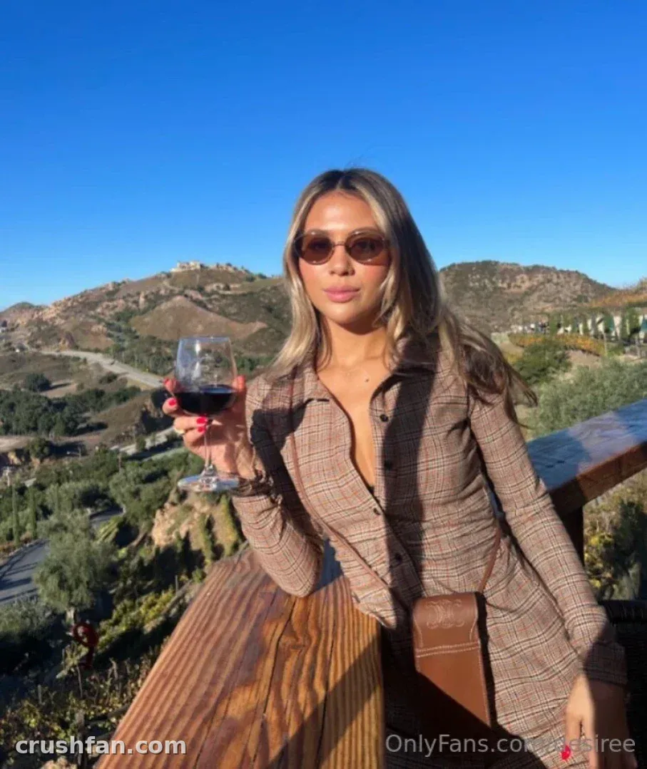 Woman in a plaid jacket and sunglasses holding a wine glass on a sunny terrace