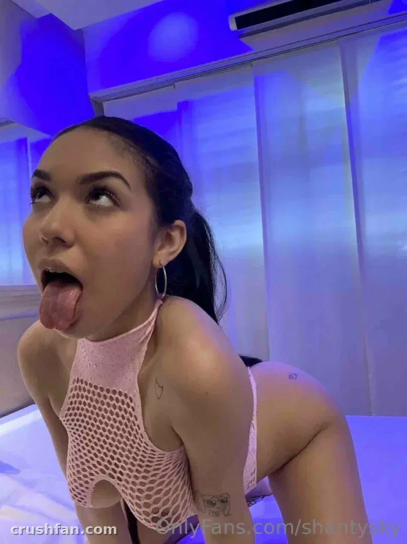 Shantal Sky in a pink mesh top on a bed under blue lighting