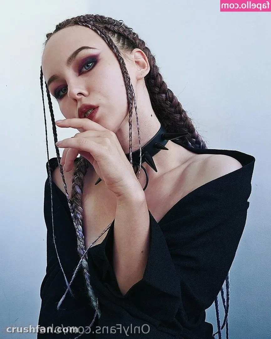 Retrato de OheekoltsOnly com cabelo trançado, maquiagem escura e uma blusa preta ombro a ombro.