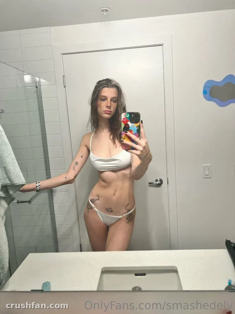 Smashedely macht ein Spiegel-Selfie in einem weißen Zweiteiler in einem hellen Badezimmer.
