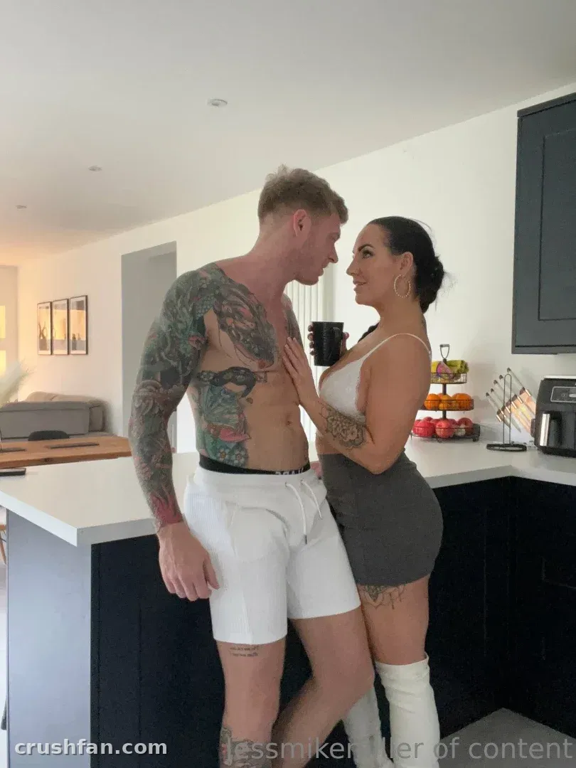 Jess Miller in a white top and grey skirt standing beside a shirtless tattooed man in a kitchen