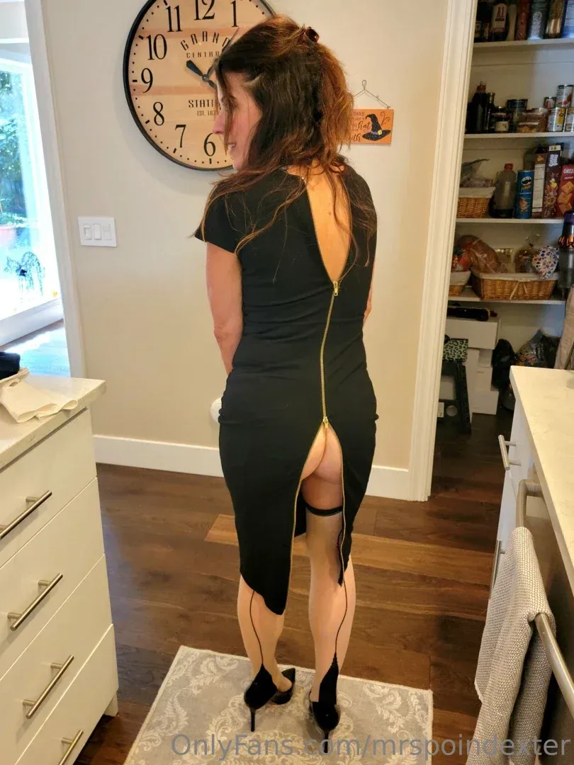 Mrs. Poindexter in a black dress with a gold zipper standing in a home interior.