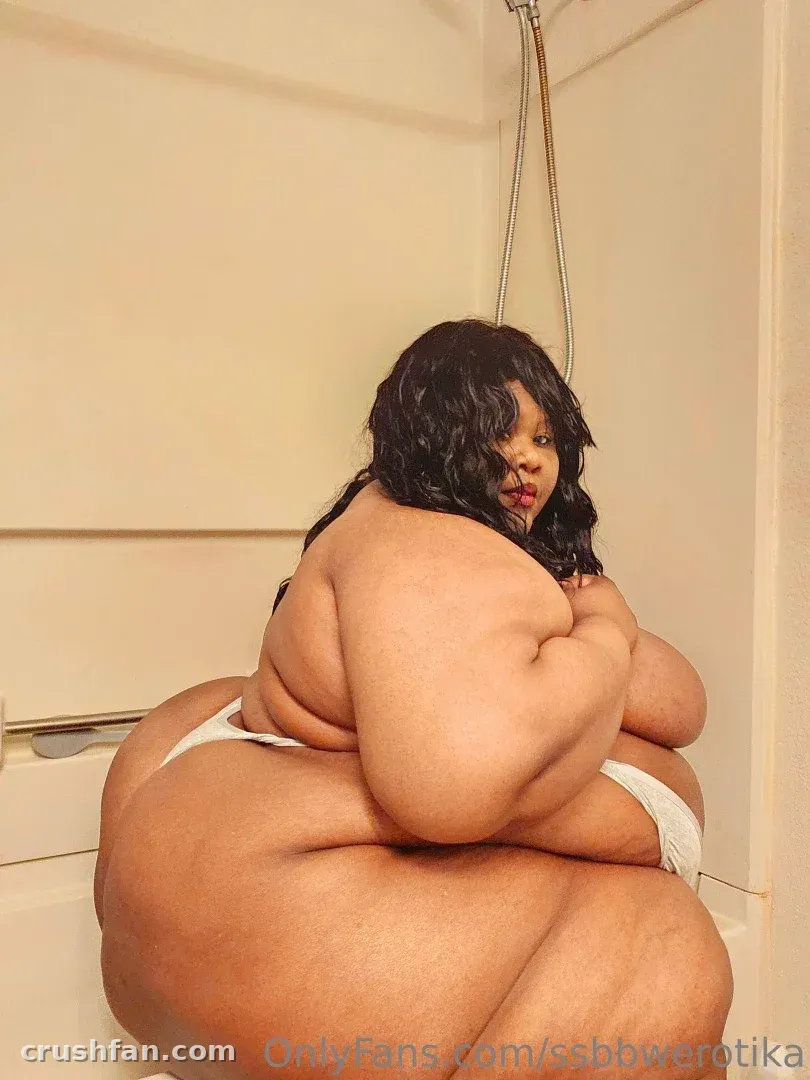 Erotika seated in a bright bathroom wearing white lingerie