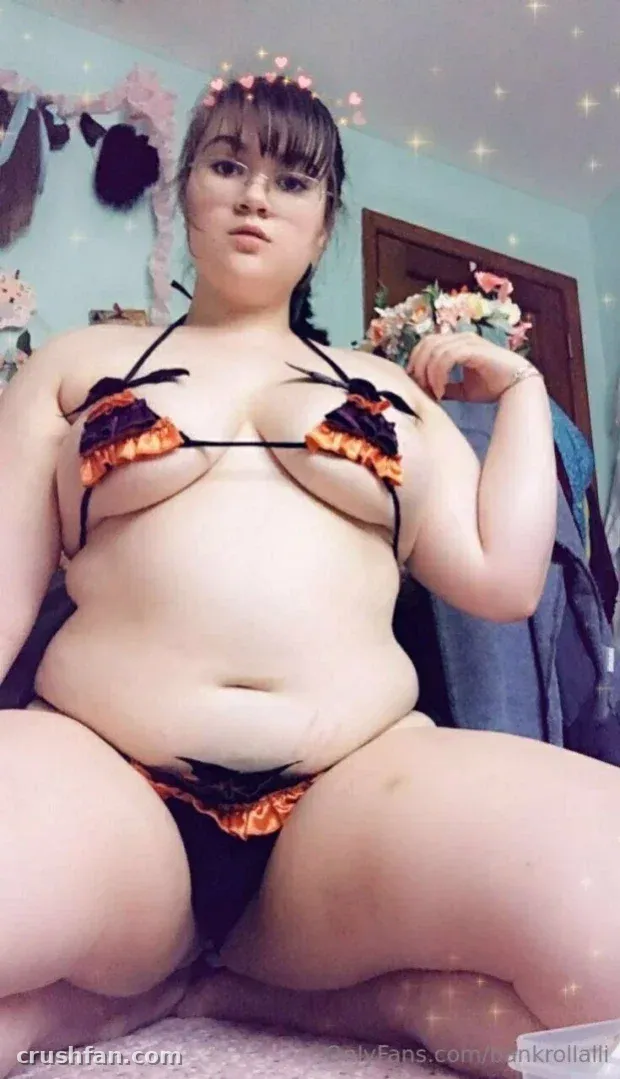 Criadora com um conjunto de duas peças franzido preto e laranja sentada em um quarto iluminado com luzes de fio.
