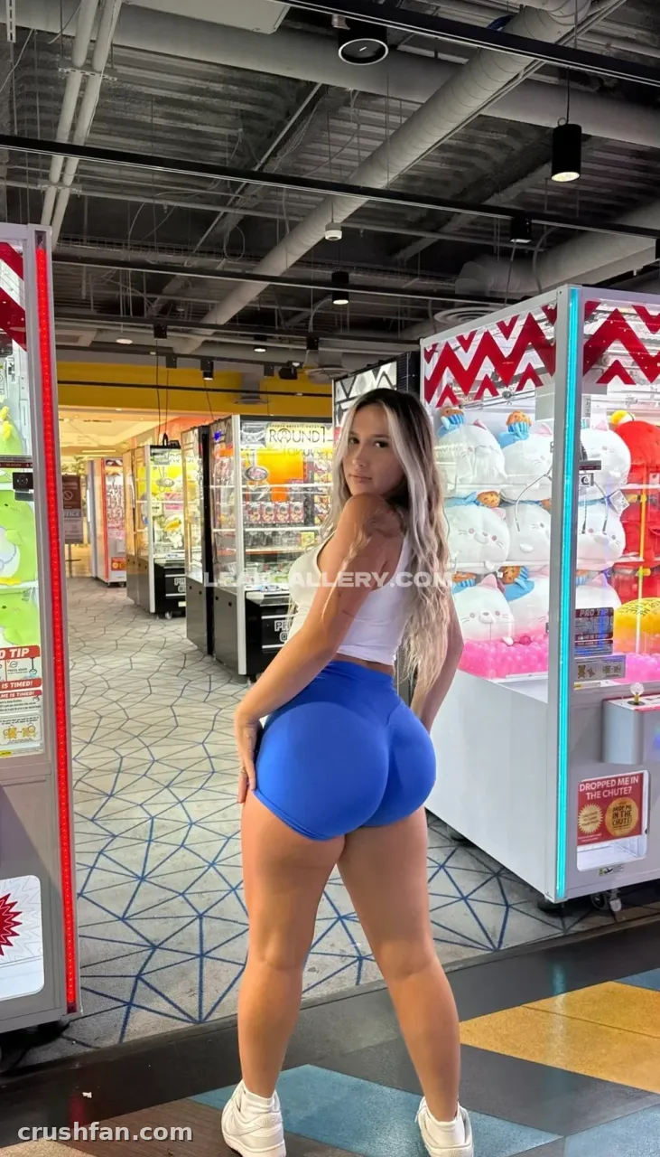 Azra Ramic com top branco e shorts azuis em pé em um fliperama colorido com máquinas de garra