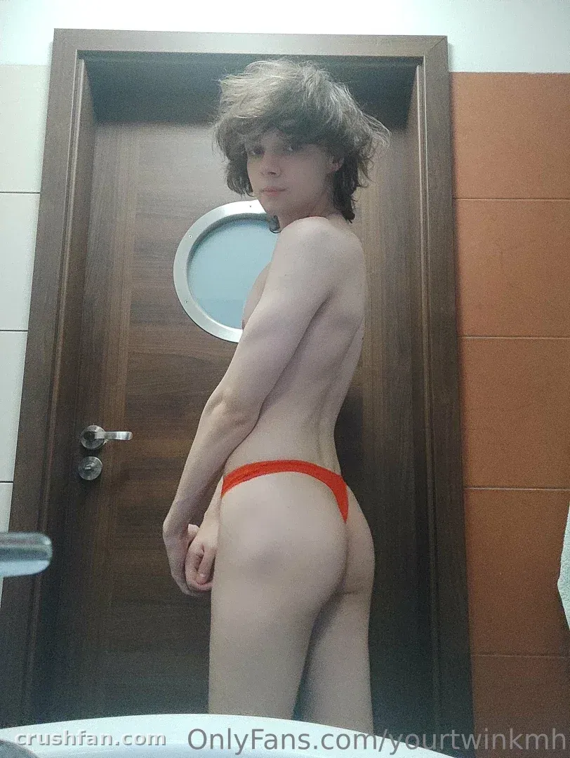 Creator in red briefs standing sideways beside a wooden door with a round window