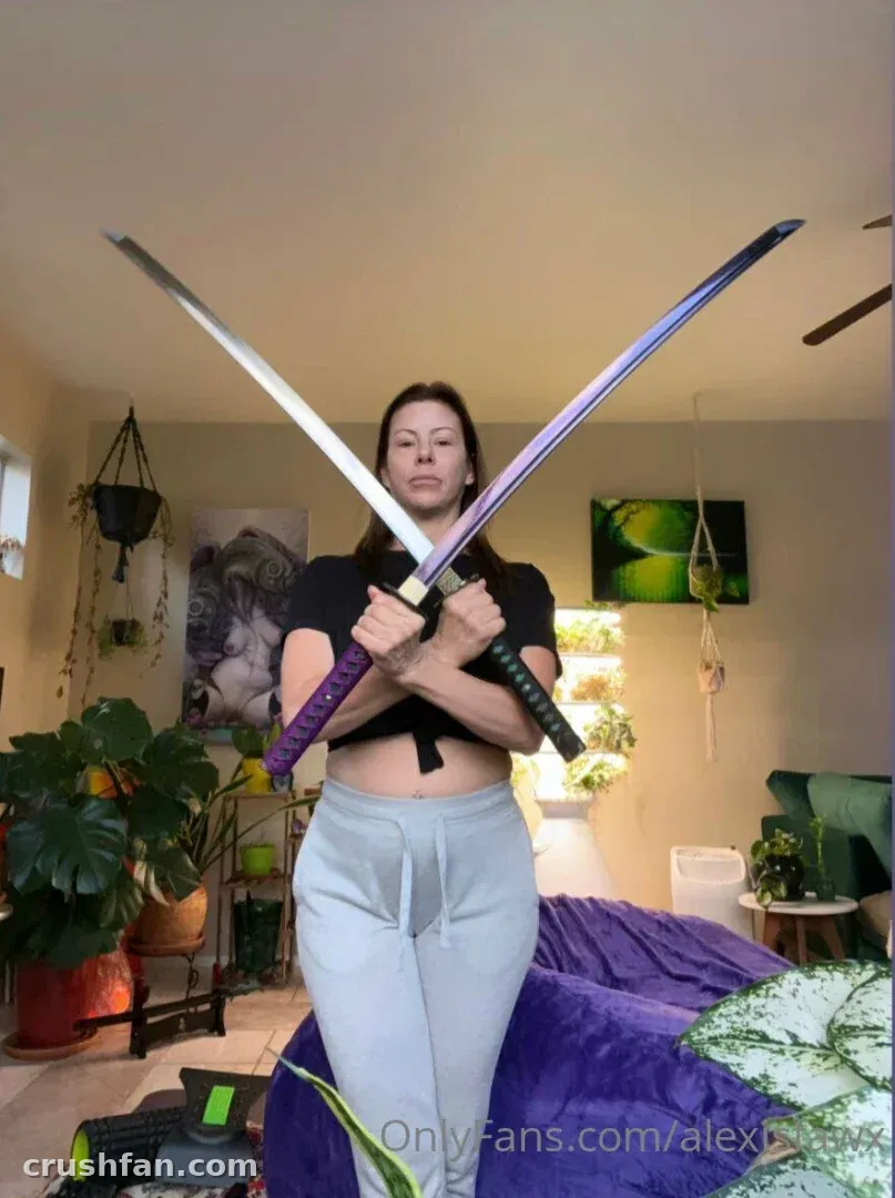 Alexis Fawx tenant deux épées croisées dans un salon avec des plantes et un canapé violet