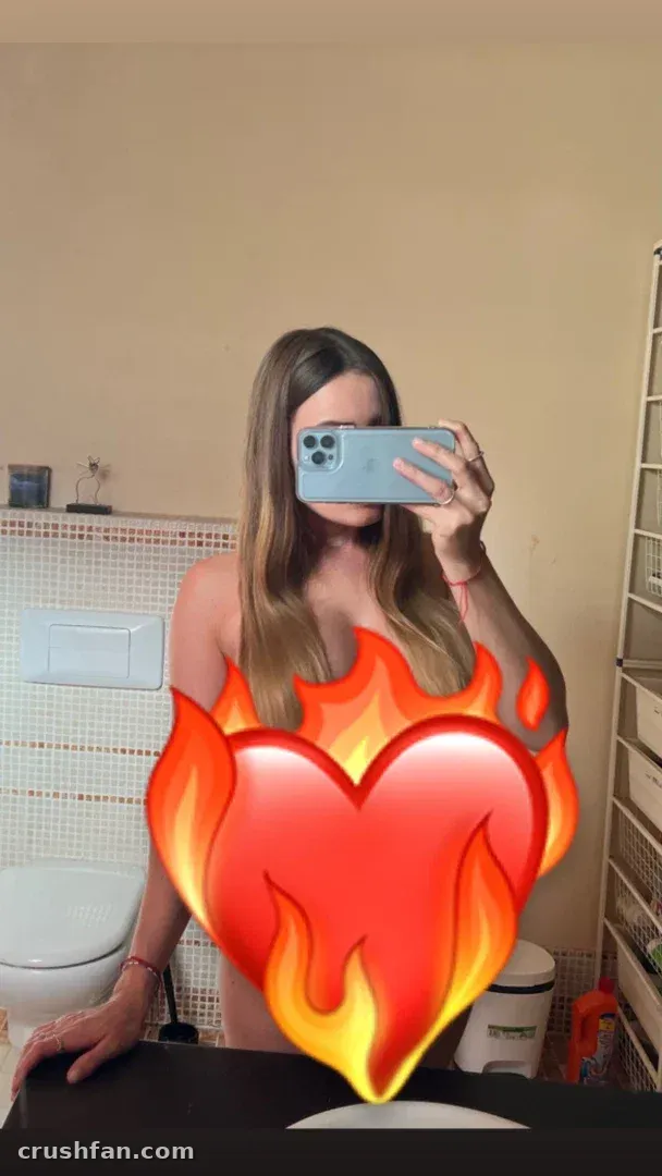 Leena Hakkinen nimmt ein Spiegel-Selfie in einem Badezimmer mit einem Flammenherz-Grafikelement auf.