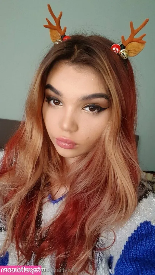 Retrato em close-up de uma mulher com cabelo ondulado cor de cobre usando chifres de rena festivos e um suéter de tricô em creme e azul.