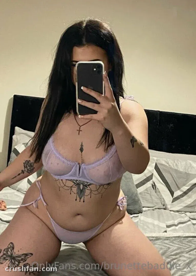 Olivia Mae taking a mirror selfie in a lilac lingerie set on a bed with grey bedding