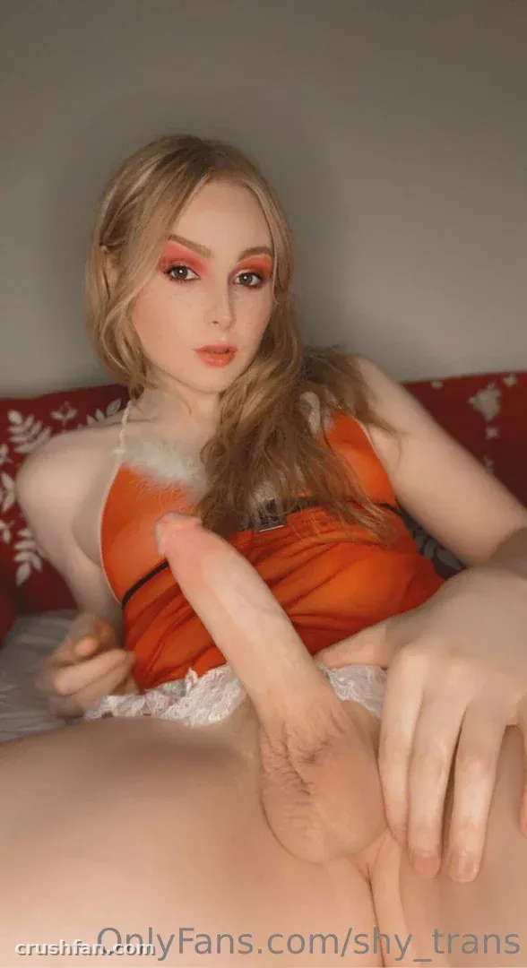 Sarah de top frente única laranja sentada em uma cama vermelha estampada com iluminação suave.