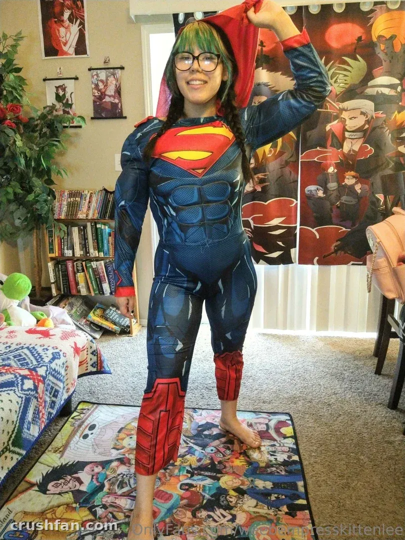 Criador em uma fantasia de super-herói azul e vermelha levantando um capuz vermelho em ambiente interno.