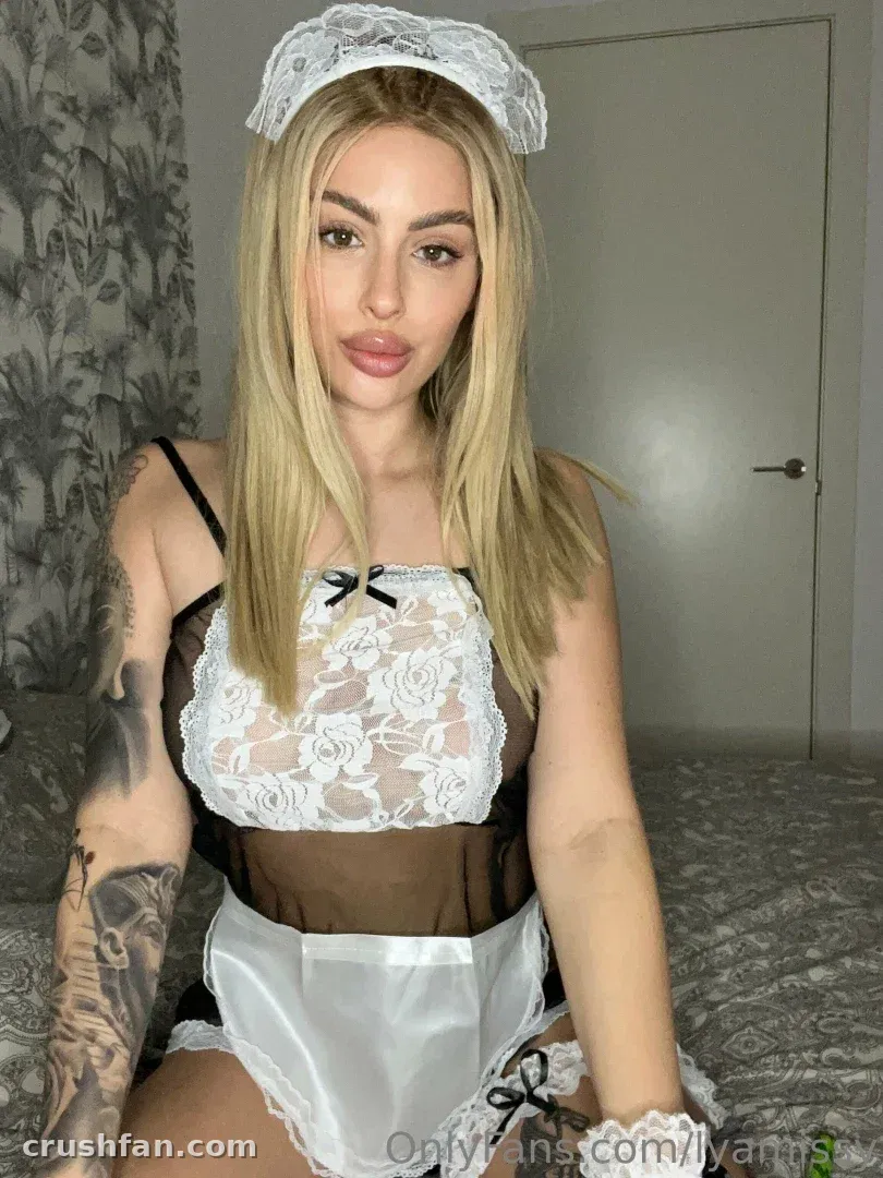 LYA MISSY in a black and white lace maid outfit seated indoors