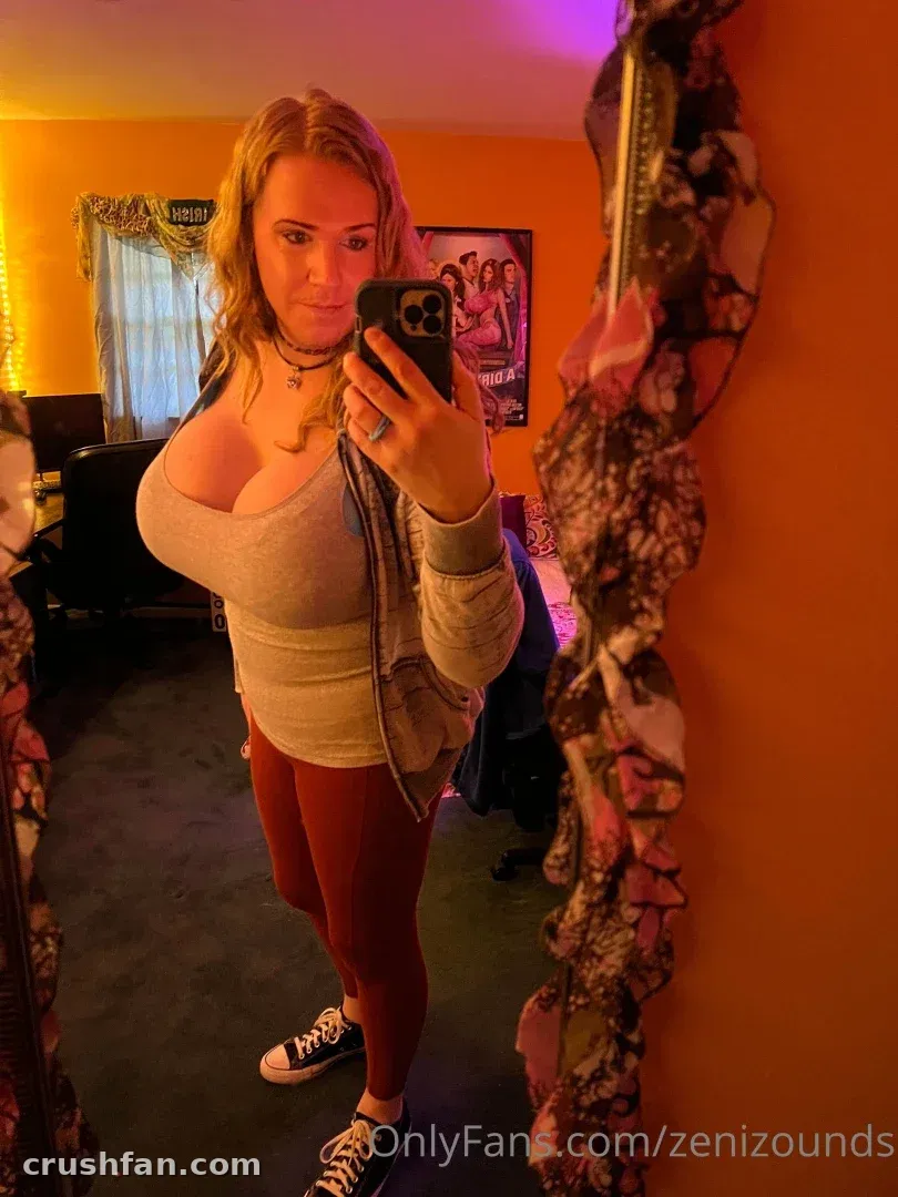 Creator in a grey top and rust leggings taking a mirror selfie in a warm-lit room