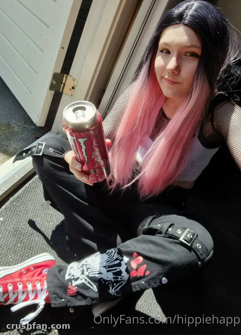 Happy assise sur des marches en extérieur tenant une canette rouge, portant un pantalon noir et des baskets rouges